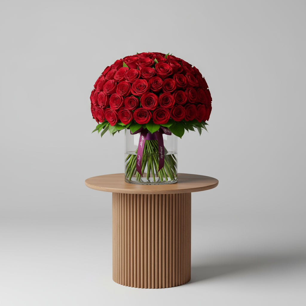 100 Red Roses Clear Vase arrangement featuring vibrant red blooms and lush green leaves