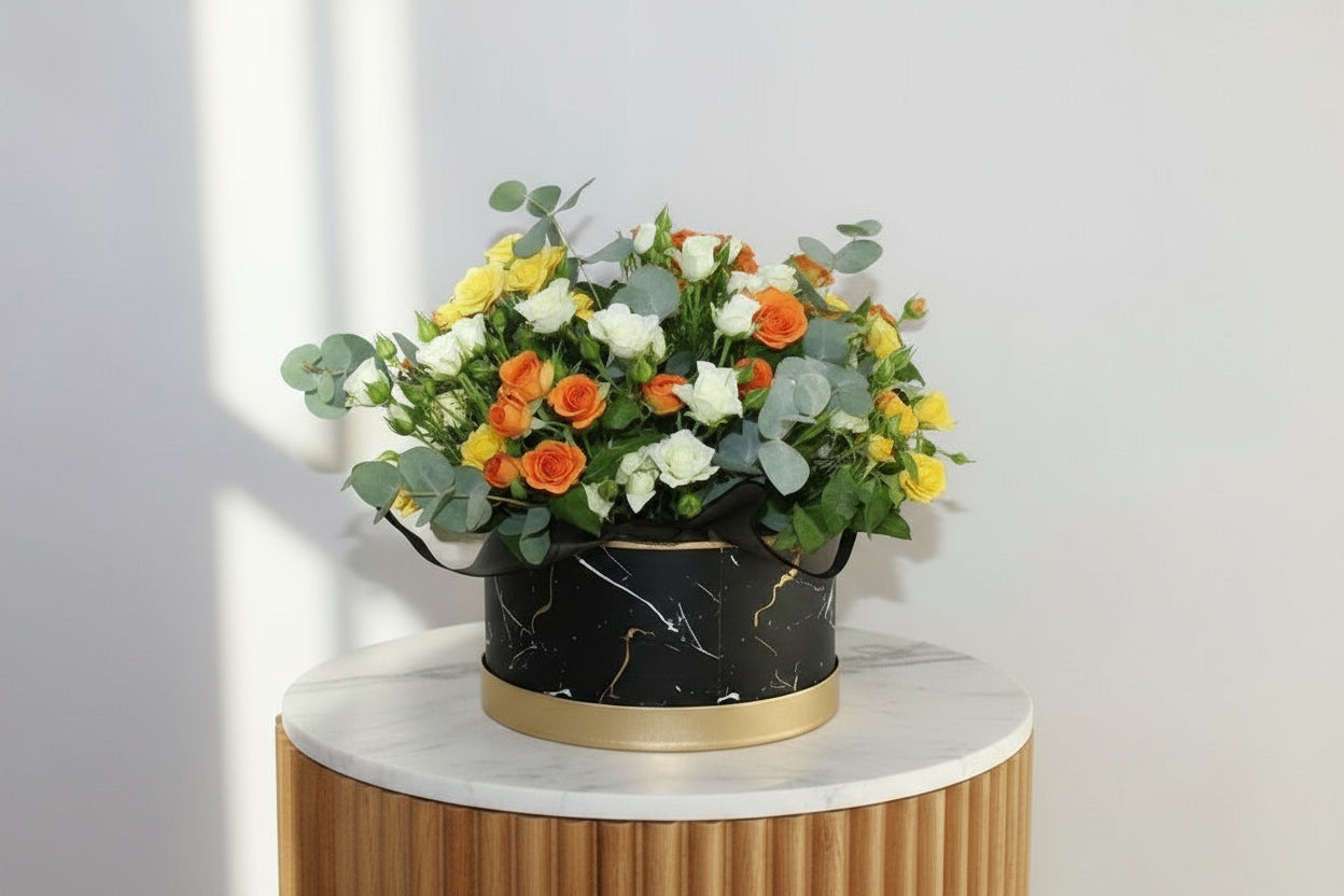 Floral arrangement in a black and gold container on a white surface with a light gray background