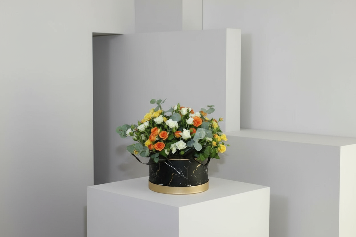 Floral arrangement in a black container on a white pedestal against a gray wall.