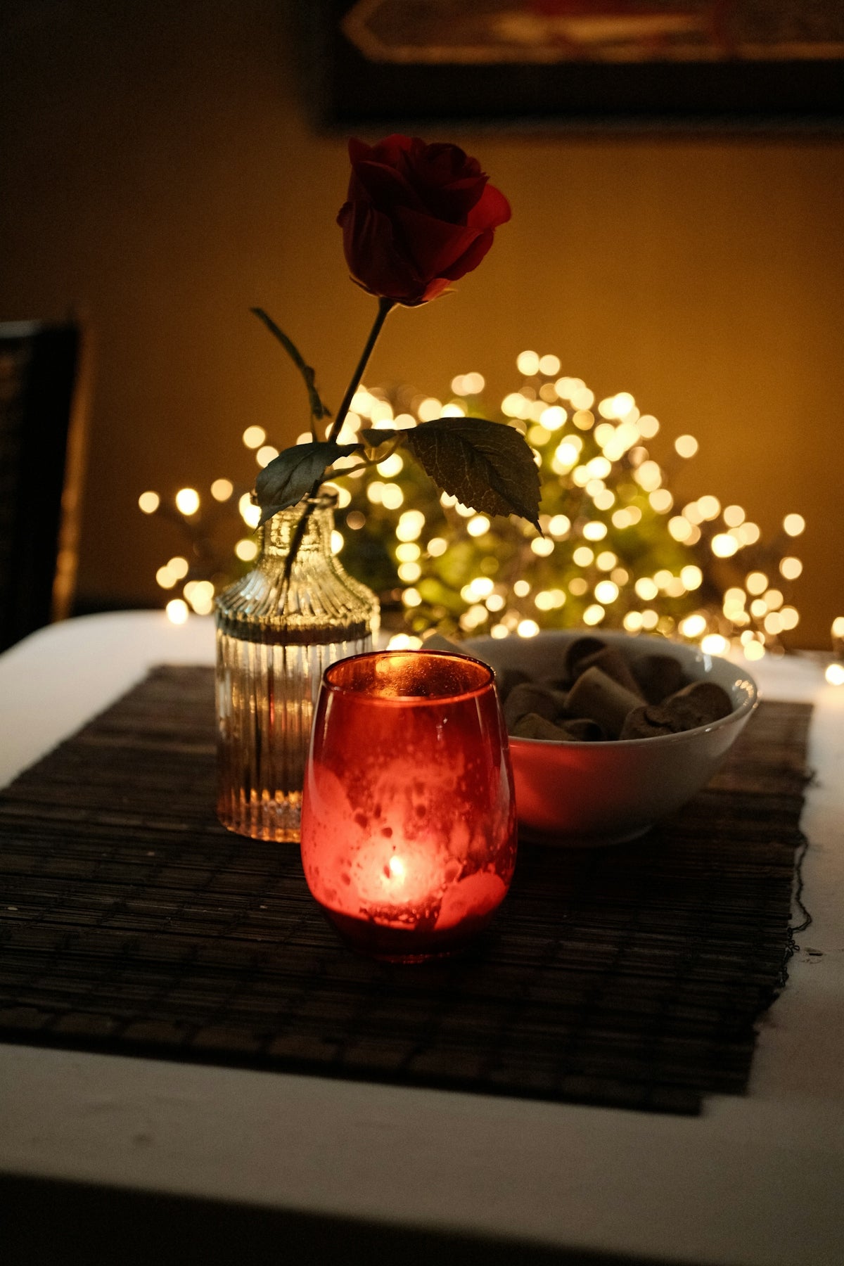 A single red rose and candle with bokeh lights
