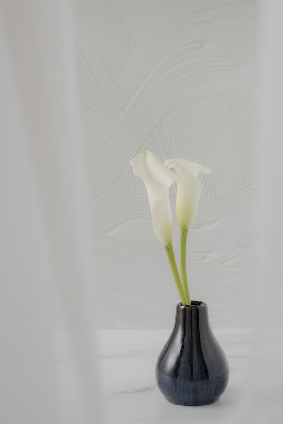 Two white calla lilies in a dark blue vase.