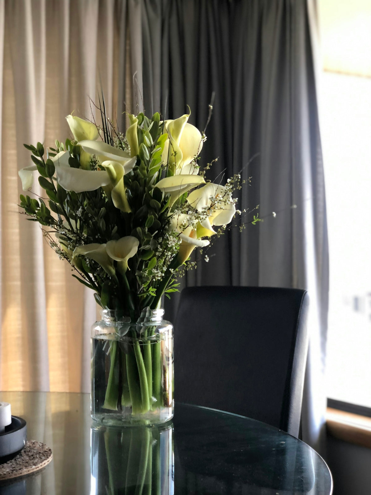 Elegant white calla lily bouquet on a reflective glass table.