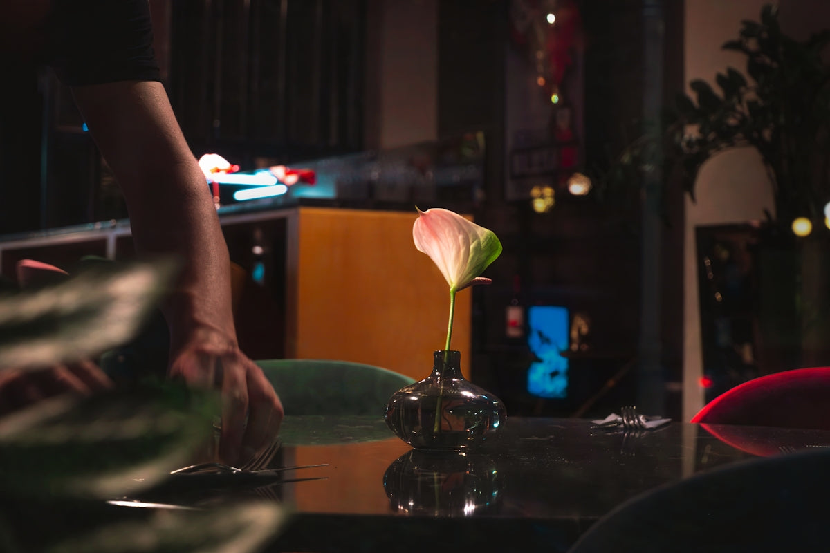 Anthurium flower in a vase on a dark, reflective table.