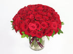 100 Red Roses Clear Vase arrangement featuring vibrant red blooms and lush green leaves