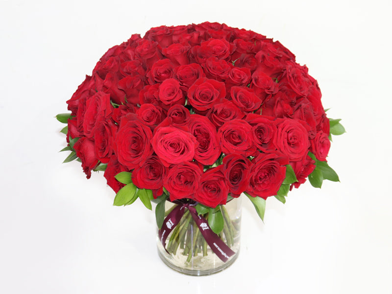 100 Red Roses Clear Vase arrangement featuring vibrant red blooms and lush green leaves
