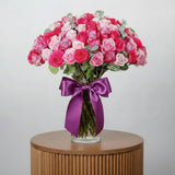 Bouquet of pink and white roses in a clear vase with a purple ribbon on a white background