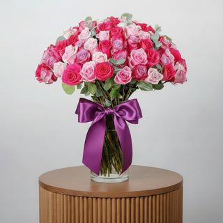 Bouquet of pink and white roses in a clear vase with a purple ribbon on a white background