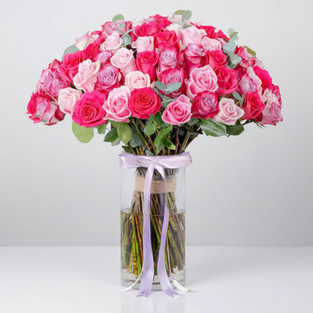 Bouquet of pink and white roses in a clear vase with a purple ribbon on a white background