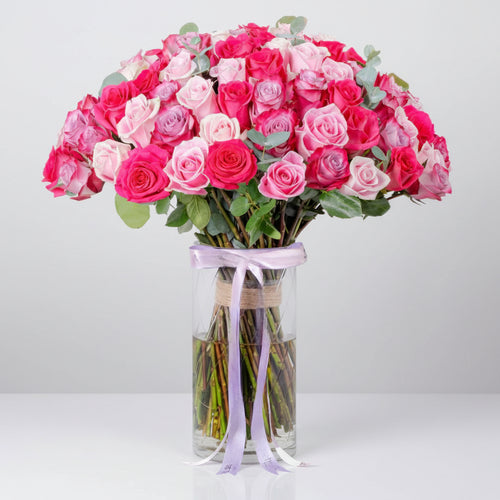 Bouquet of pink and white roses in a clear vase with a purple ribbon on a white background