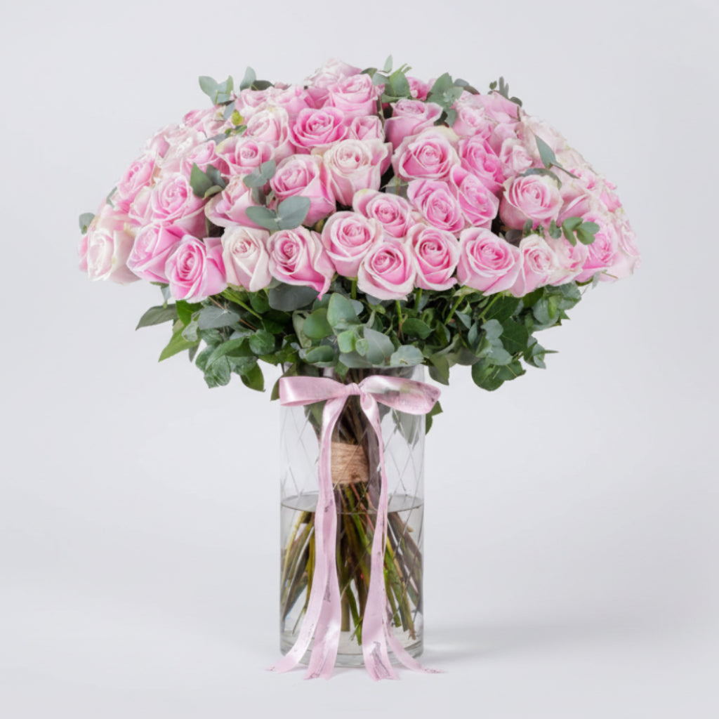 Bouquet of pink roses in a clear vase with a pink ribbon on a white background