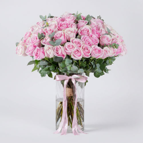Bouquet of pink roses in a clear vase with a pink ribbon on a white background