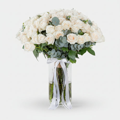 Bouquet of white roses with greenery in a clear vase on a white background
