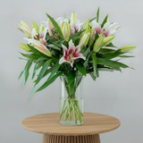 Bouquet of pink and white lilies in a clear vase on a white surface with a light gray background