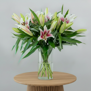 Bouquet of pink and white lilies in a clear vase on a white surface with a light gray background