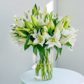 Bouquet of white lilies in a clear vase on a table with a neutral background