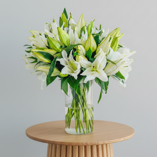 Bouquet of white lilies in a clear vase on a table with a neutral background