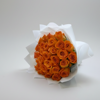A bouquet of vibrant orange roses wrapped in white paper, placed on a white marble surface with a soft beige curtain background.