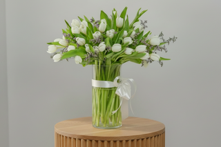 Bouquet of 40 white tulips in a clear vase with a white ribbon