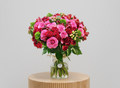 Bouquet of pink and red roses with greenery in a clear vase on a white background