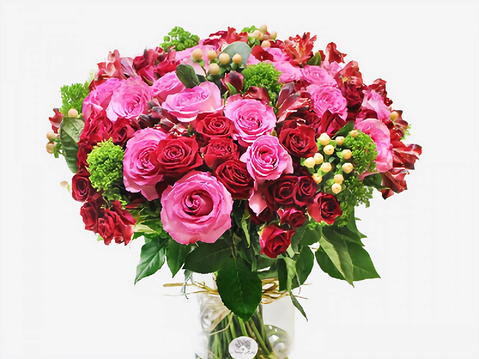 Bouquet of pink and red roses with greenery in a clear vase on a white background
