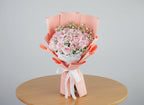 Bouquet of pink roses with baby's breath wrapped in pink paper on a wooden table with a gray background
