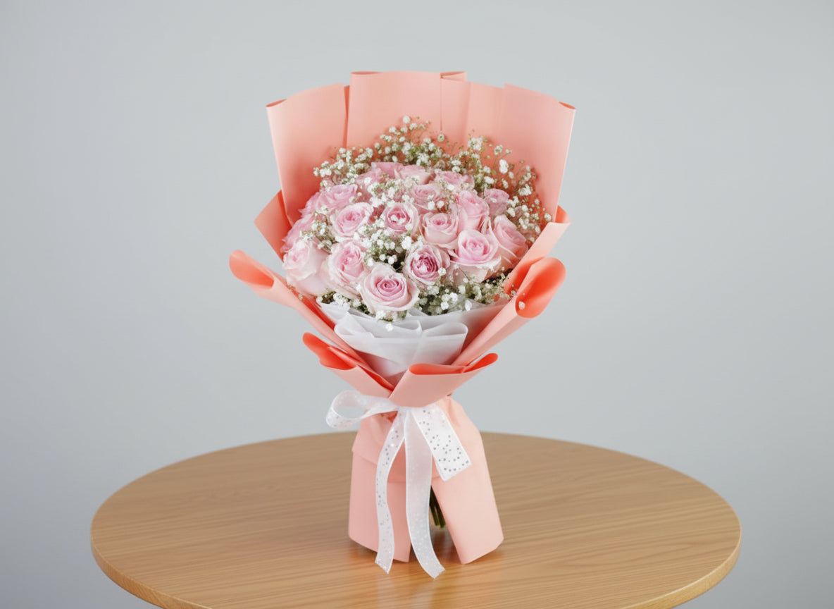 Bouquet of pink roses with baby's breath wrapped in pink paper on a wooden table with a gray background