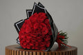 Bouquet of red roses wrapped in black paper with a red ribbon on a white table.