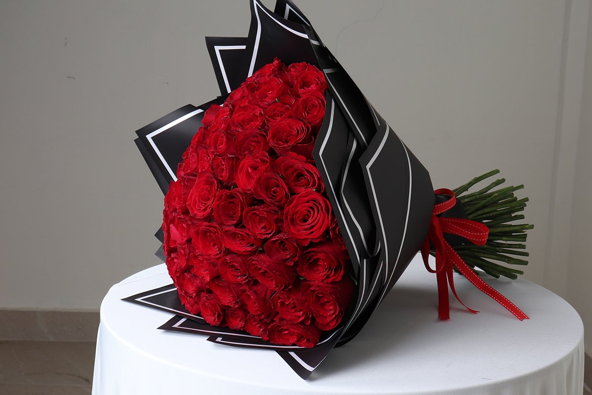 Bouquet of red roses wrapped in black paper with a red ribbon on a white table.