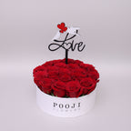 Box of red roses with a 'Love' sign and 'Pooji Flowers' branding