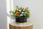 Floral arrangement in a black and gold container on a white surface with a light gray background