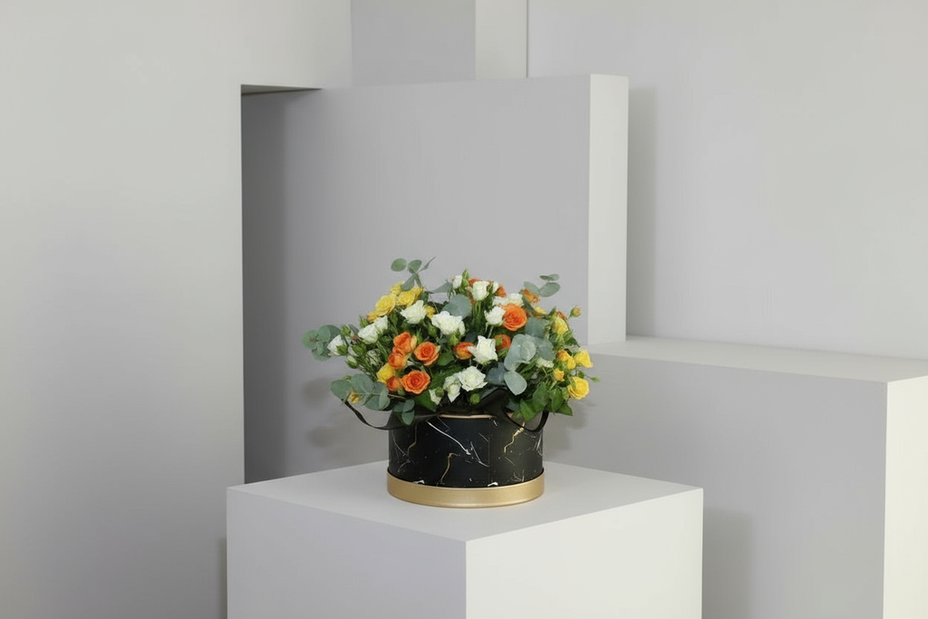 Floral arrangement in a black container on a white pedestal against a gray wall.