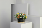 Floral arrangement in a black container on a white pedestal against a gray wall.