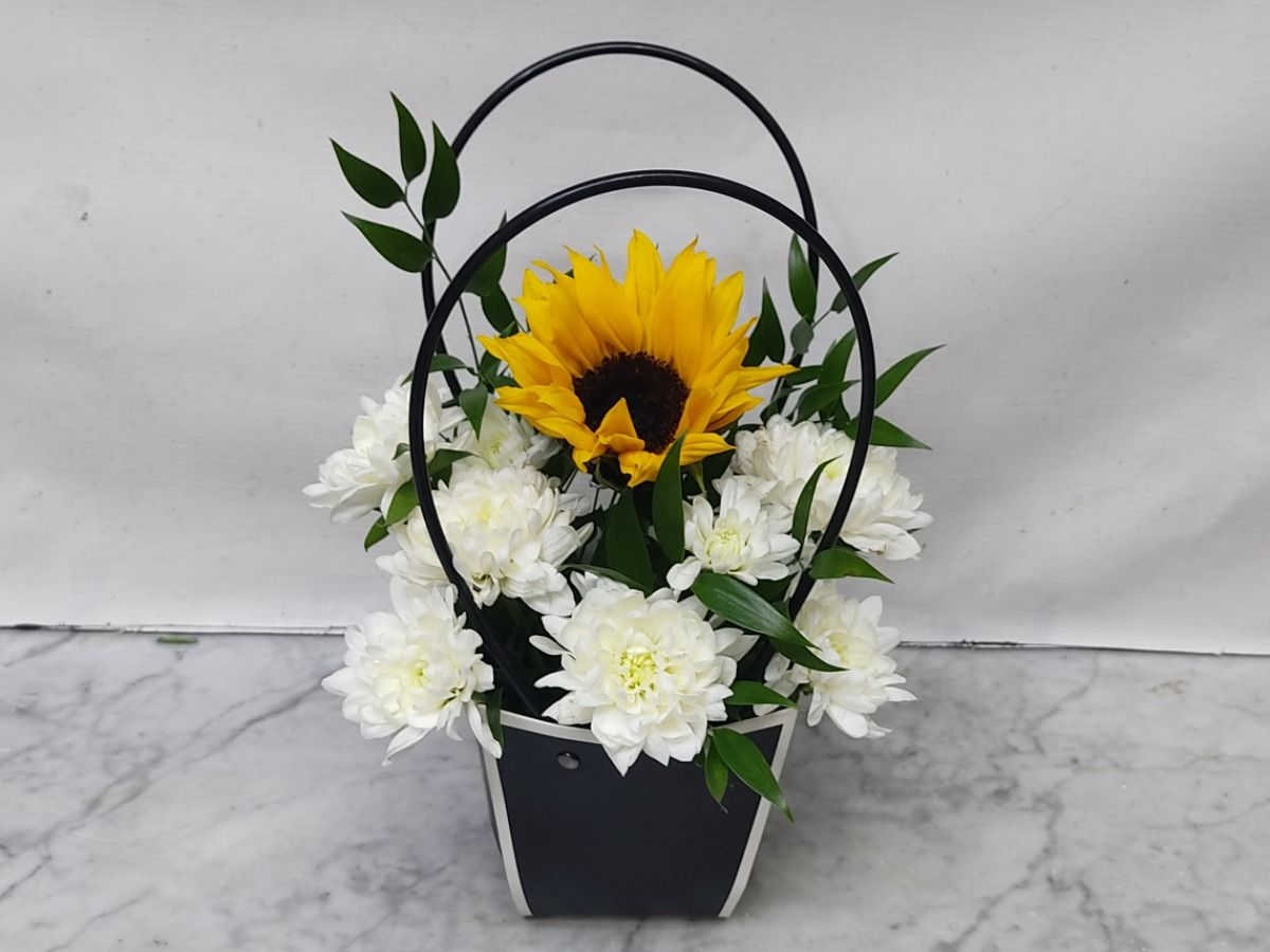 Floral arrangement with a sunflower and white flowers in a black basket on a marble surface.