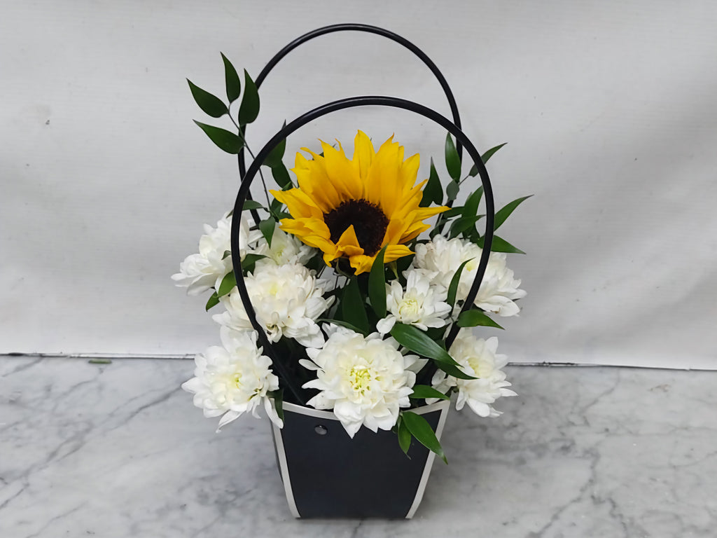 Floral arrangement with a sunflower and white flowers in a black basket on a marble surface.