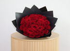Bouquet of red roses wrapped in black paper on a wooden stand with a white background