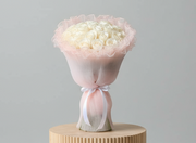 Hand bouquet containing white roses with pink wrapping paper.