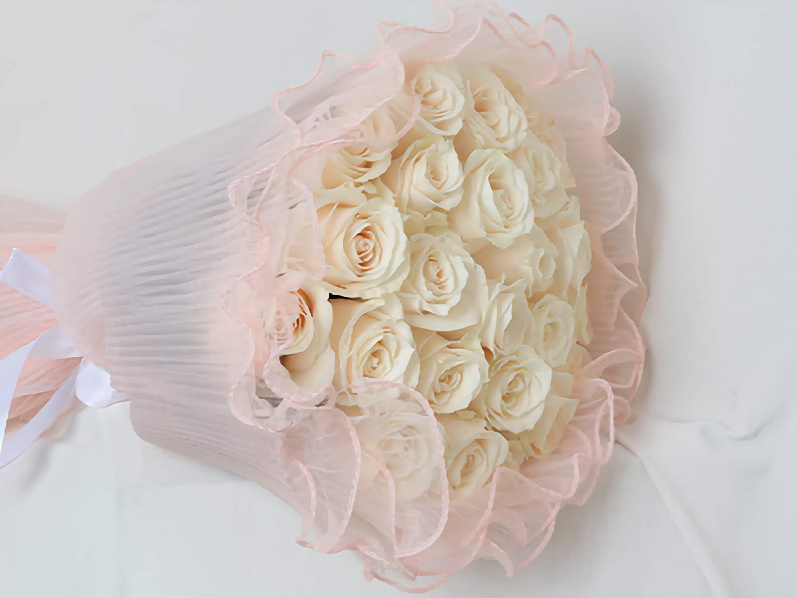 Hand bouquet containing white roses with pink wrapping paper.