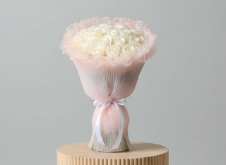 Hand bouquet containing white roses with pink wrapping paper.