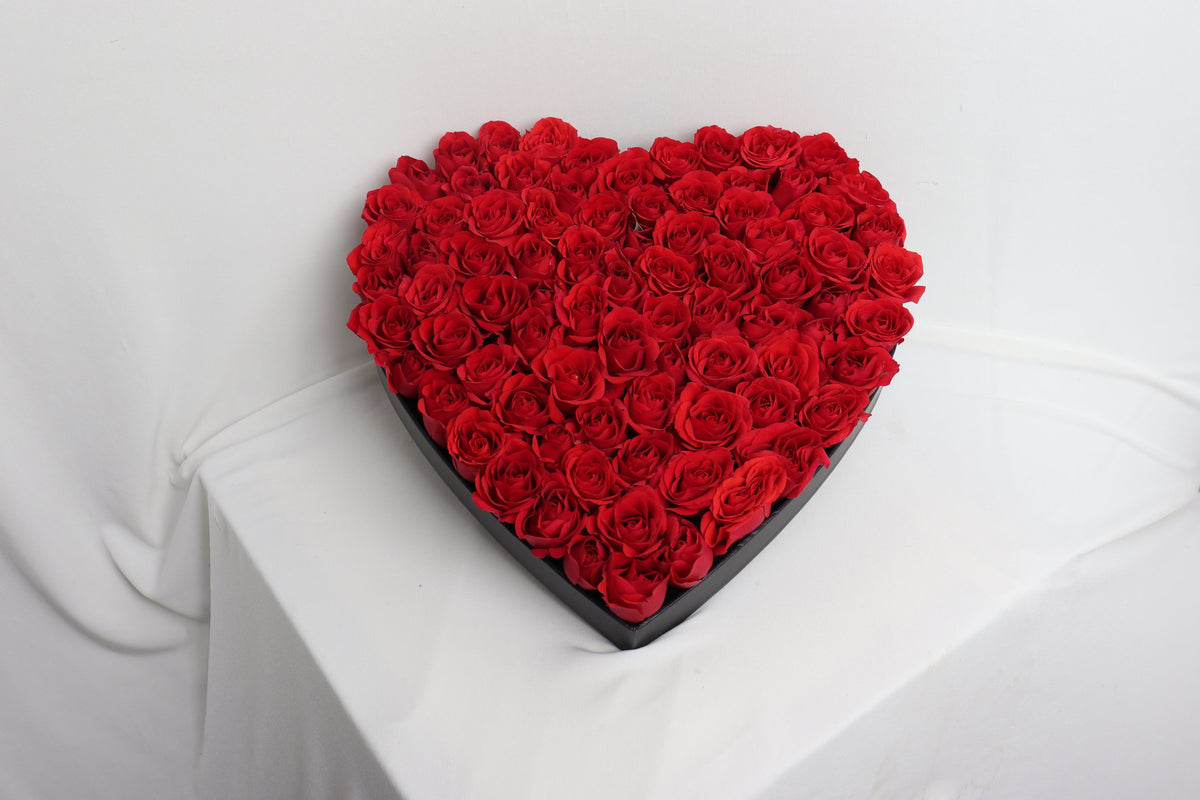 Heart-shaped arrangement of red baby roses on a white surface