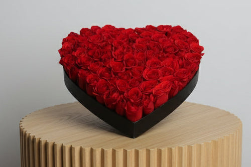 Heart-shaped arrangement of red baby roses on a white surface
