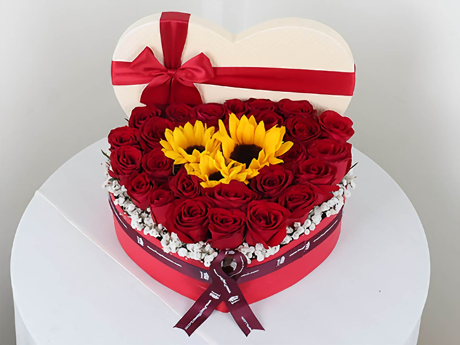 Heart-shaped flower arrangement with red roses and sunflowers on a white background