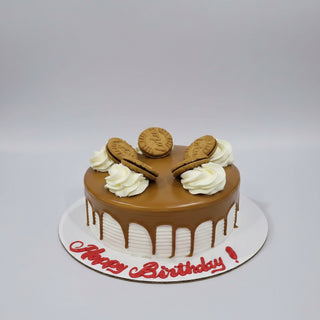 A round birthday cake with glossy brown chocolate glaze, decorated with white piped cream swirls and five biscuit cookies. The cake sits on a white board with 'Happy Birthday!' written in red icing, photographed on a gray metal surface.