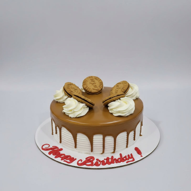 A round birthday cake with glossy brown chocolate glaze, decorated with white piped cream swirls and five biscuit cookies. The cake sits on a white board with 'Happy Birthday!' written in red icing, photographed on a gray metal surface.