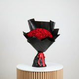 Bouquet of red roses wrapped in black paper with a red ribbon on a white background