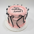 Pink birthday cake with black text and ribbons on a white background
