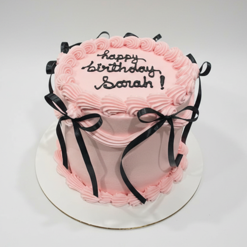 Pink birthday cake with black text and ribbons on a white background