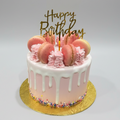Pink birthday cake with macarons and a 'Happy Birthday' topper on a white background