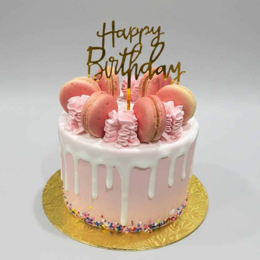 Pink birthday cake with macarons and a 'Happy Birthday' topper on a white background