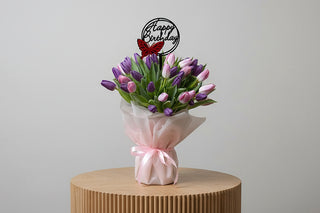 Bouquet of purple and pink tulips with a 'Happy Birthday' candle on a wooden stand.
