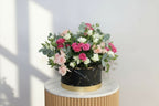 Bouquet of pink and white flowers in a black container on a light gray background